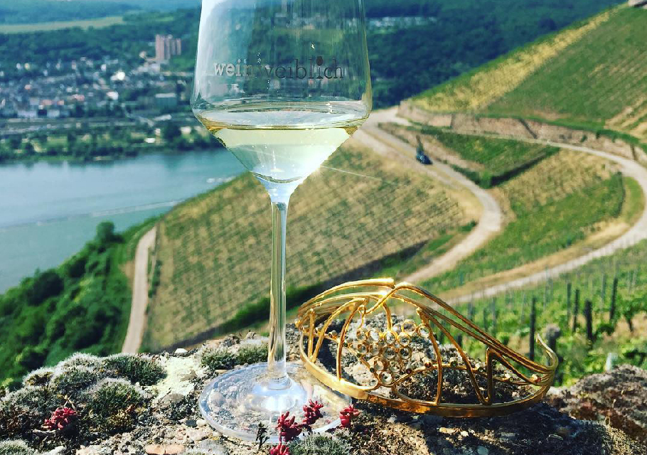 A glass of german white wine in the foreground with a steep slope of vineyard in the distance